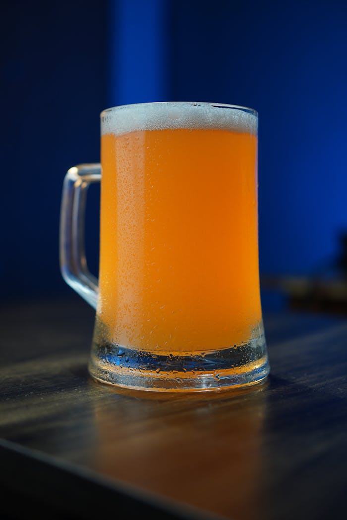 Frosty glass of orange craft beer on a wooden table with a vibrant blue background.