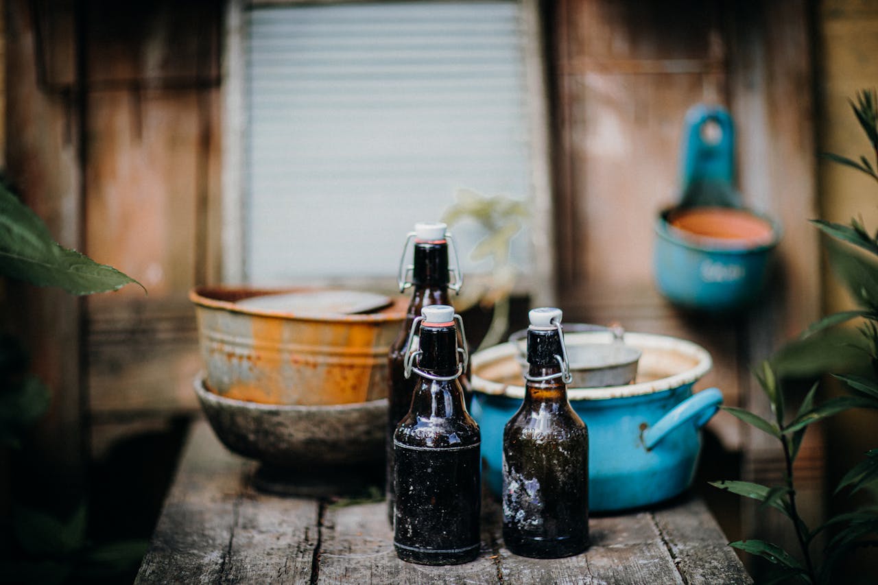 Vintage beer bottles on a rustic wooden table with old kitchenware, evoking a nostalgic countryside feel.