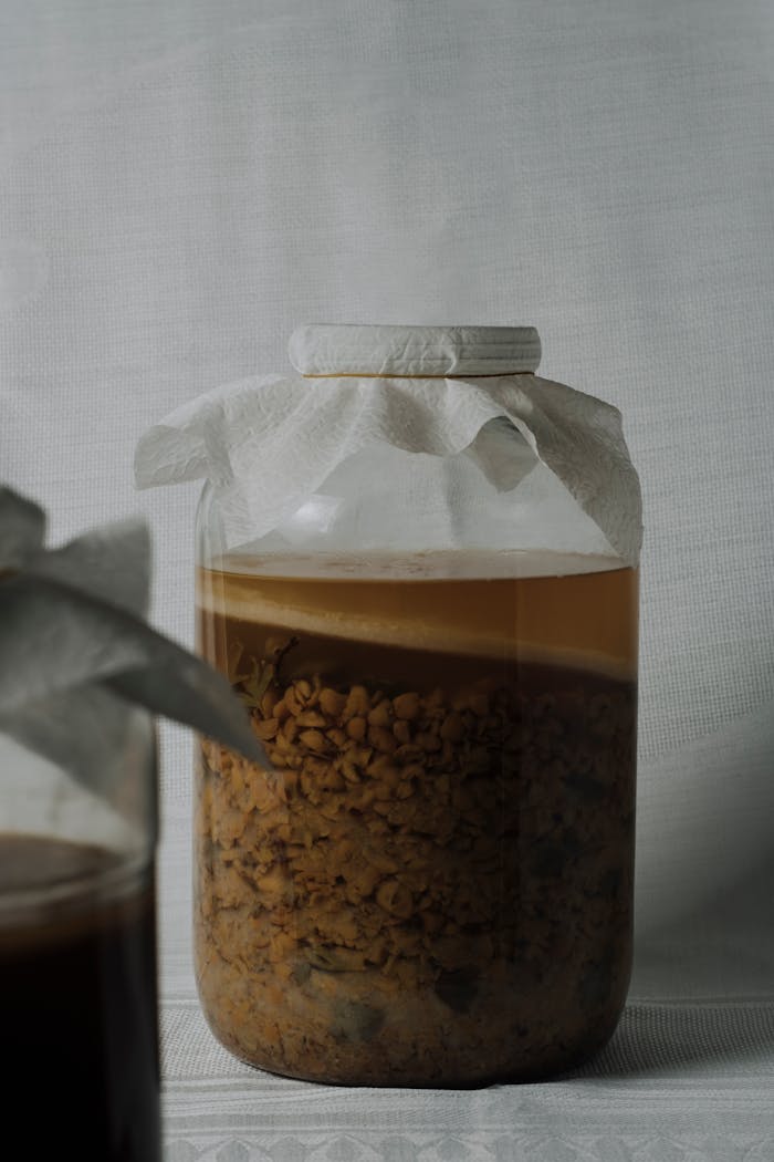 Glass jar with fermenting mixture on plain background, showcasing fermentation process.