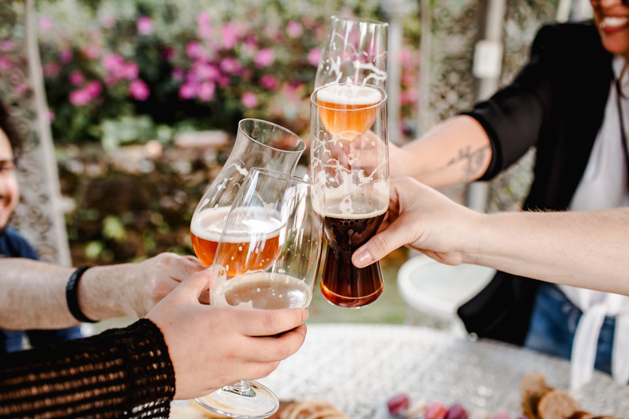 Friends raising craft beer glasses in a joyful outdoor celebration with a floral background.