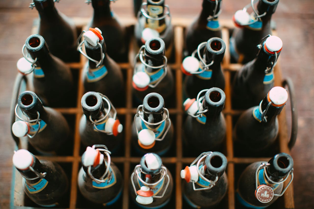 Collection of vintage glass bottles with metal caps organized in a wooden crate from above.
