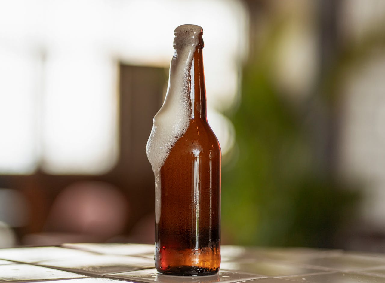 Close-up of a foaming beer bottle on a bar counter indoors.