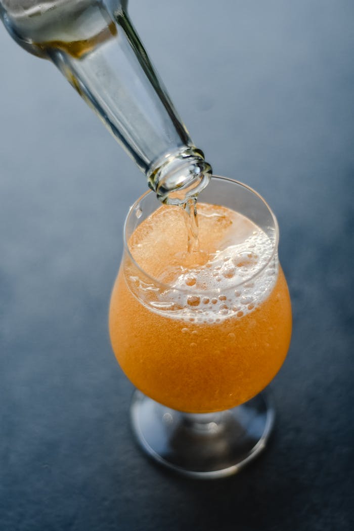 Close-up of a bright orange fizzy drink being poured into a glass on a dark background.