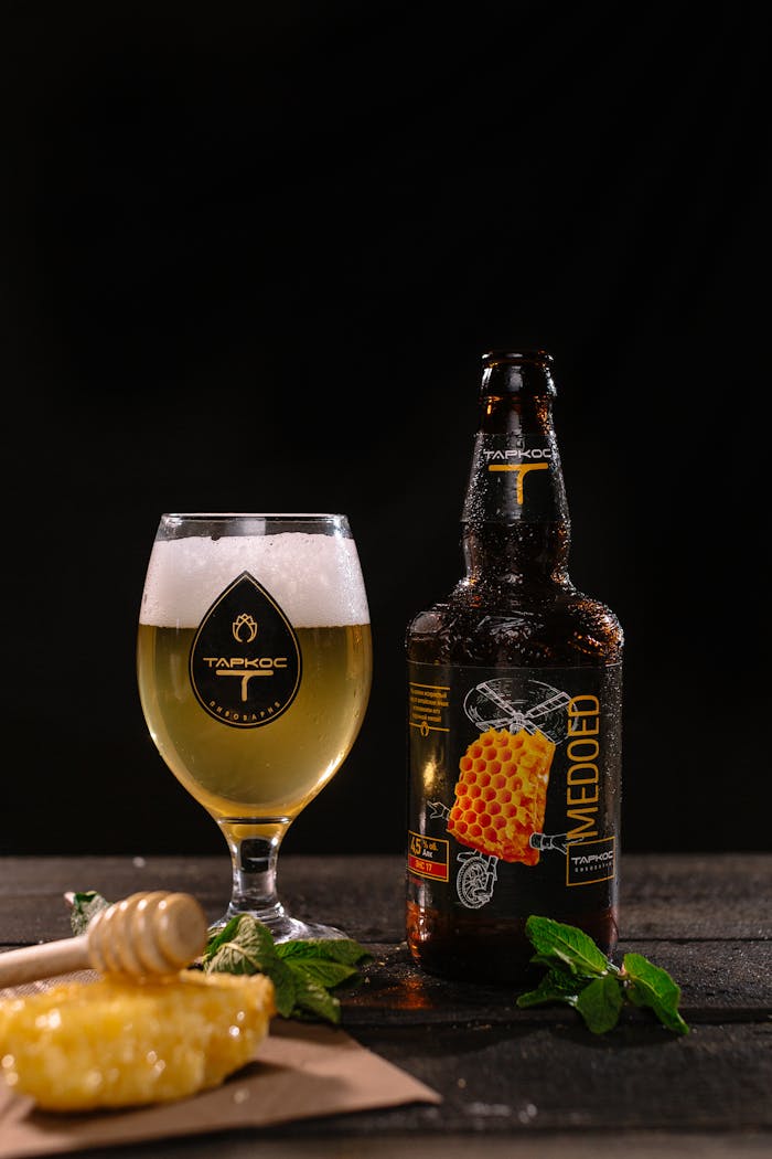 Close-up product shot of craft honey beer with basil leaves and honeycomb on dark background.